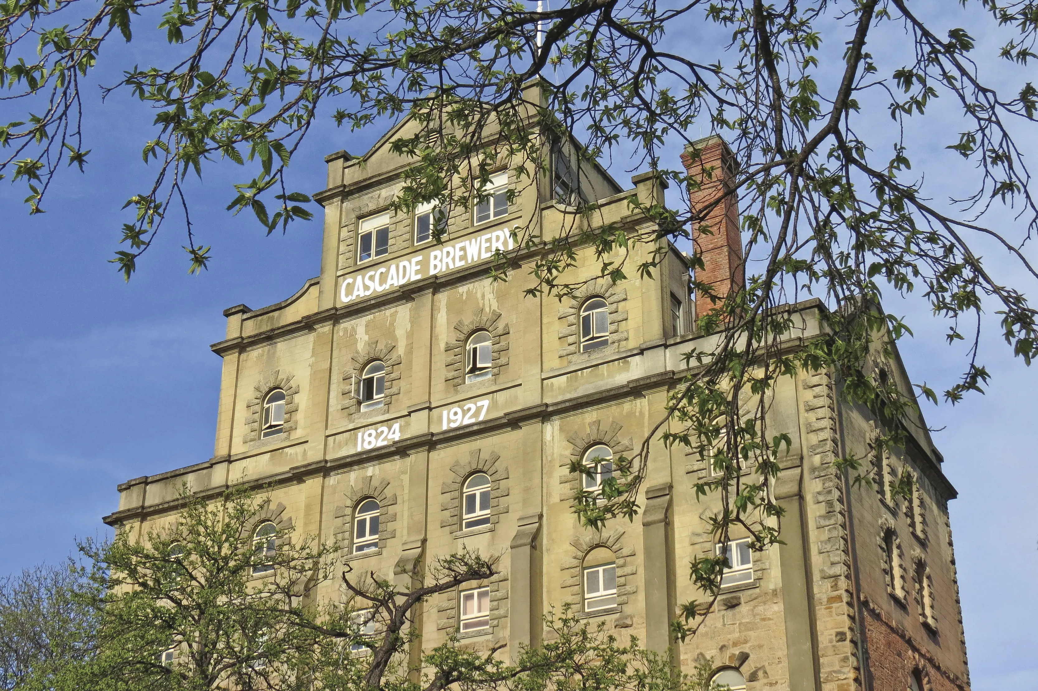 Low angle image taken outside, of the Cascade Brewery, taken through lush green trees.