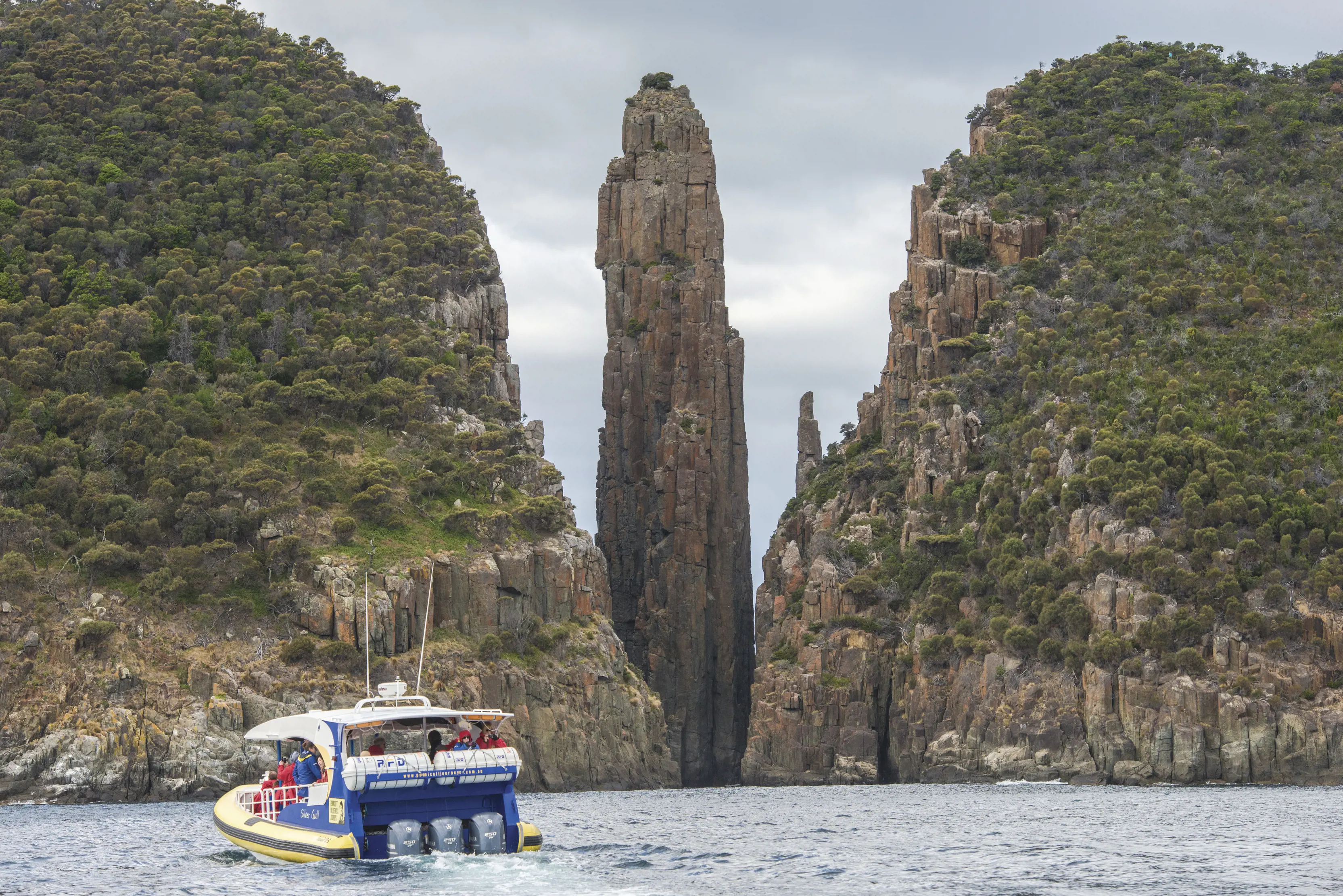 "Incredible image of a boat travelling towards near unbelievable geological formations of the cliffs and lush greenery, with Tasman Island Cruises. "