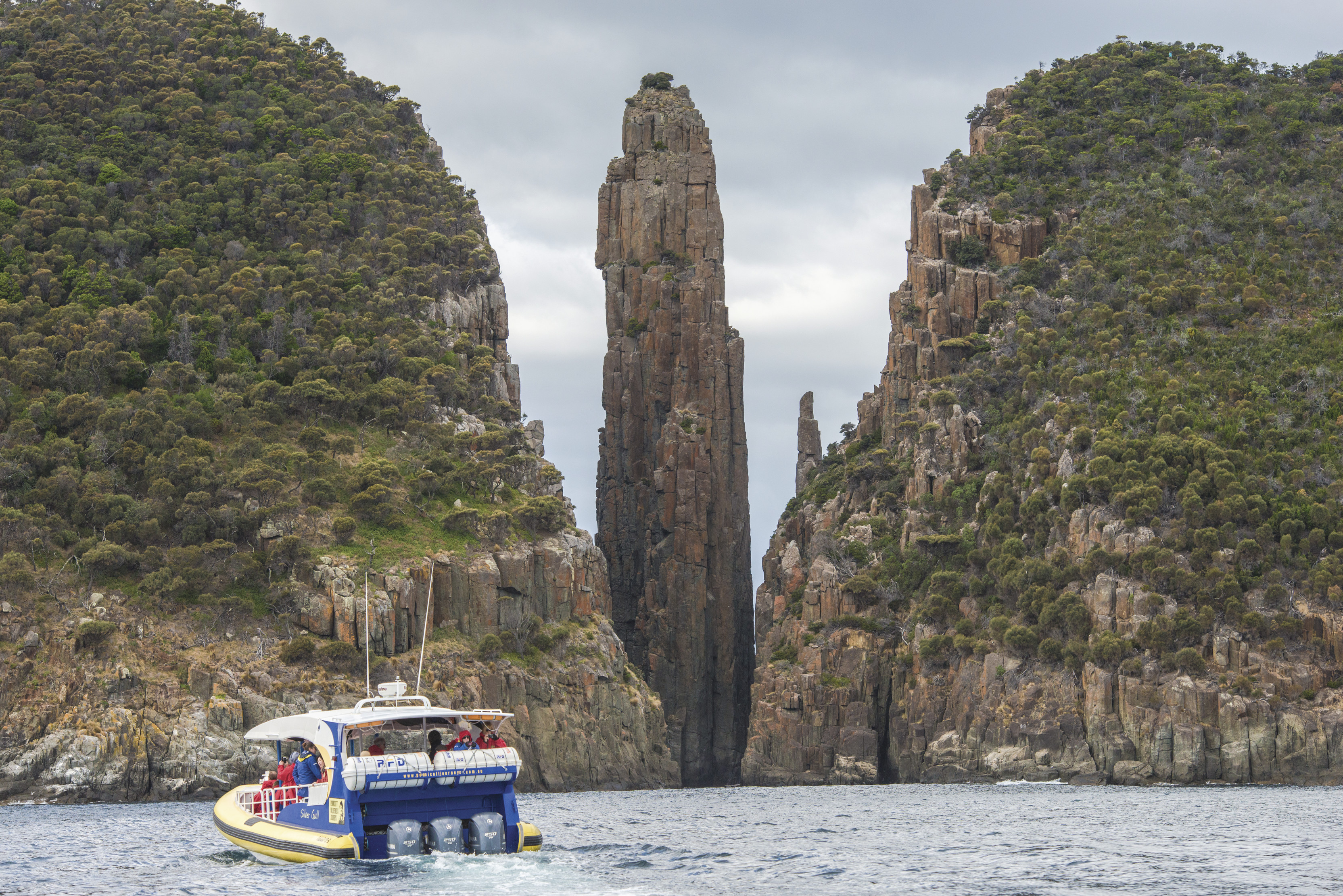 "Incredible image of a boat travelling towards near unbelievable geological formations of the cliffs and lush greenery, with Tasman Island Cruises. "