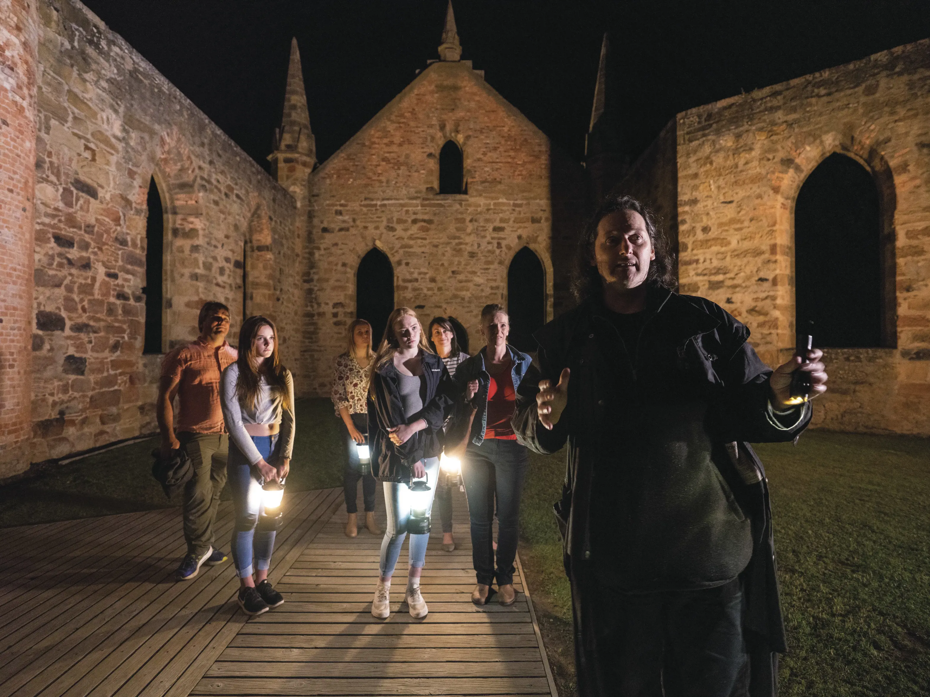 Ghost tour guide taking tourists through the historic sight at night. Tourists are holding old lamps.