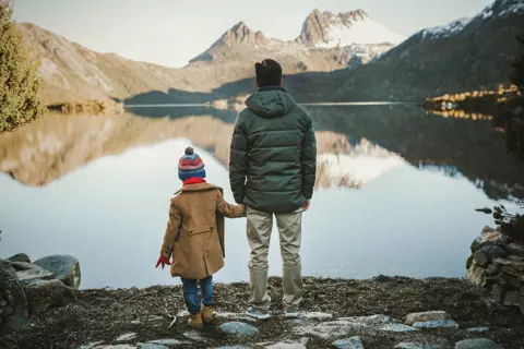 Father and son, holding hands, looking out into the incredible scenery of Cradle Mountain and the lake that lies before it. 