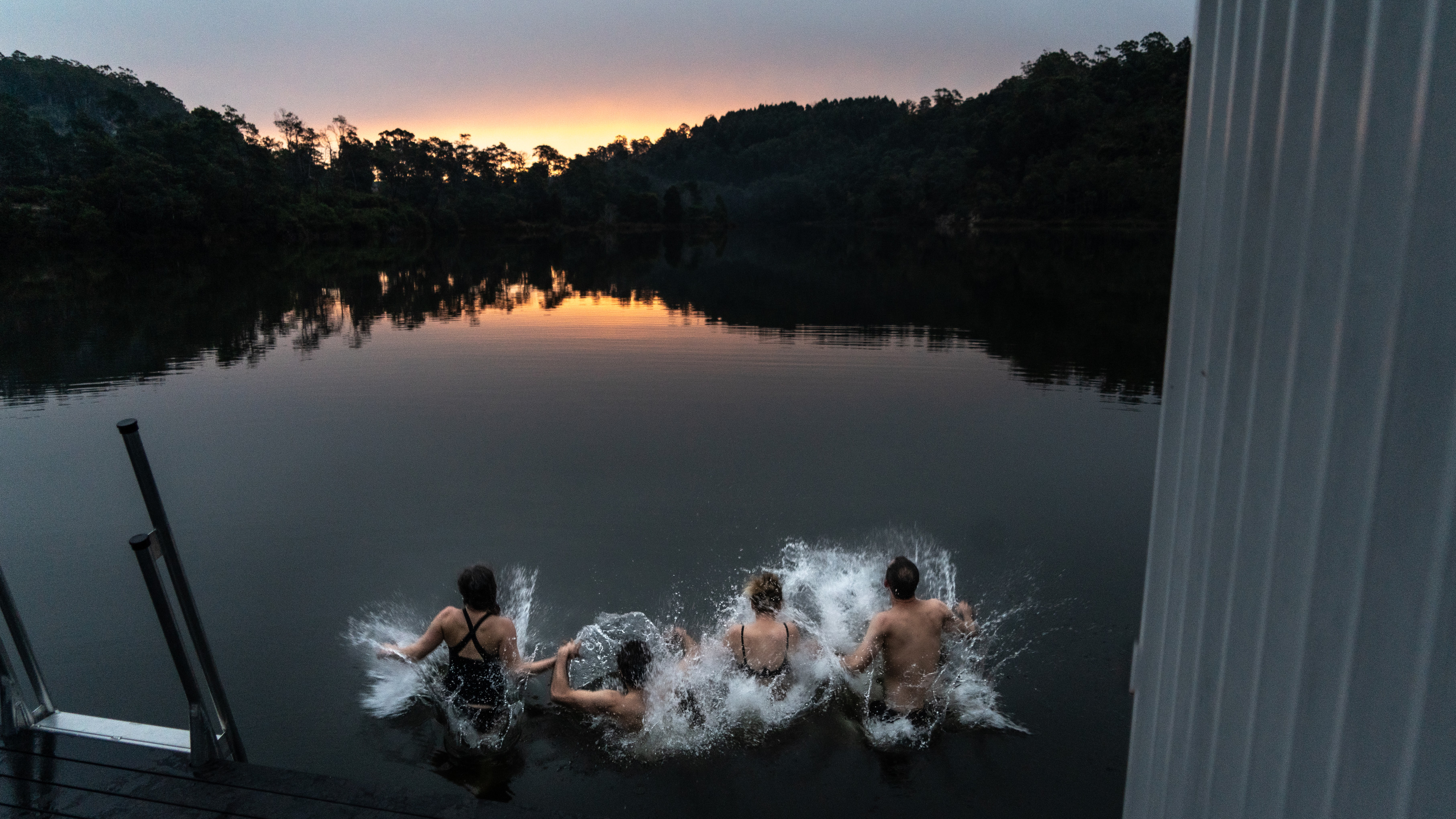 At dusk, four friends jump into the water holding hands at Floating Sauna Lake Derby.