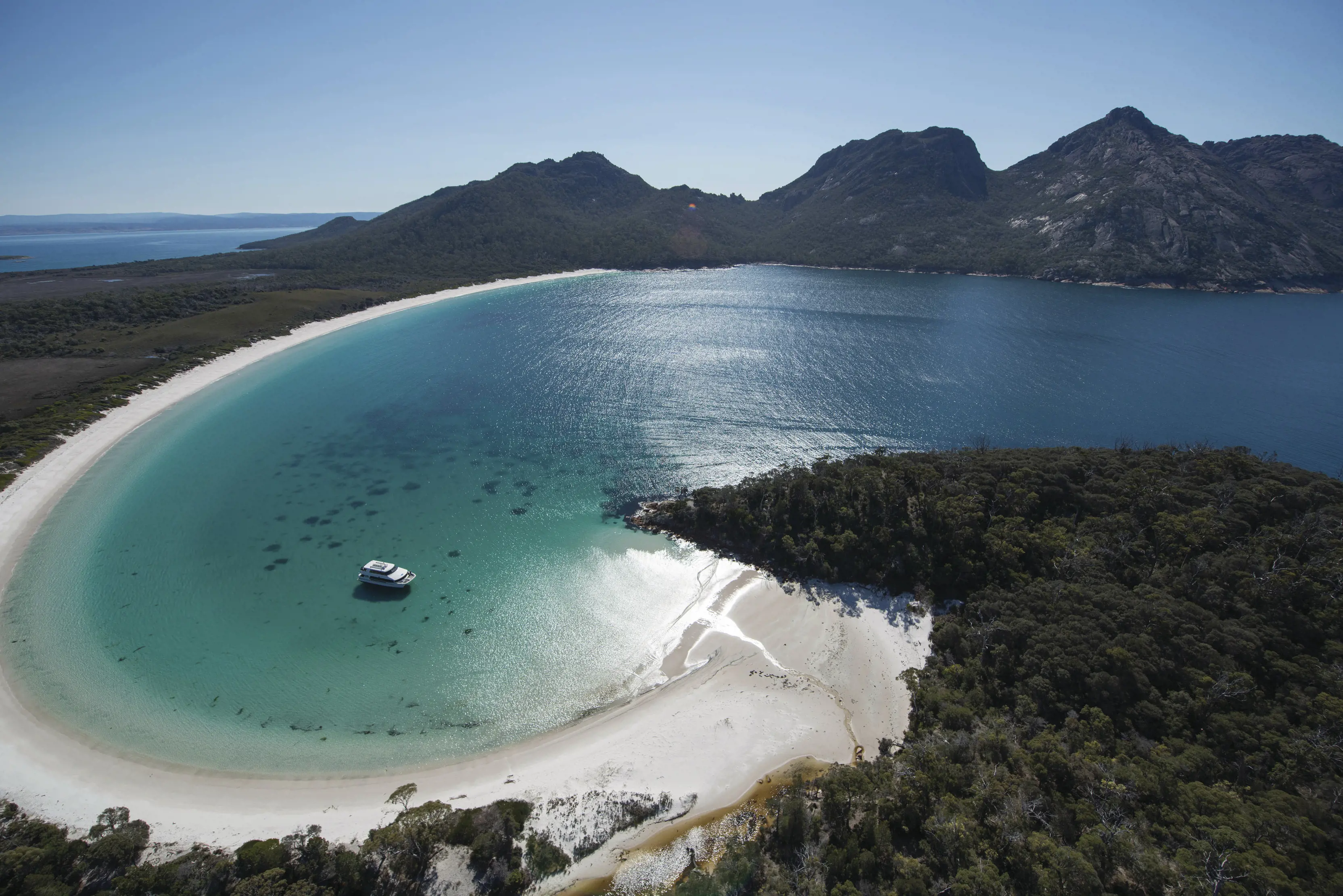 Stunning aerial image of Wineglass Bay on a clear, sunny day with crystal clear, blue water. Wineglass Bay Cruise boat is docked within the Bay.