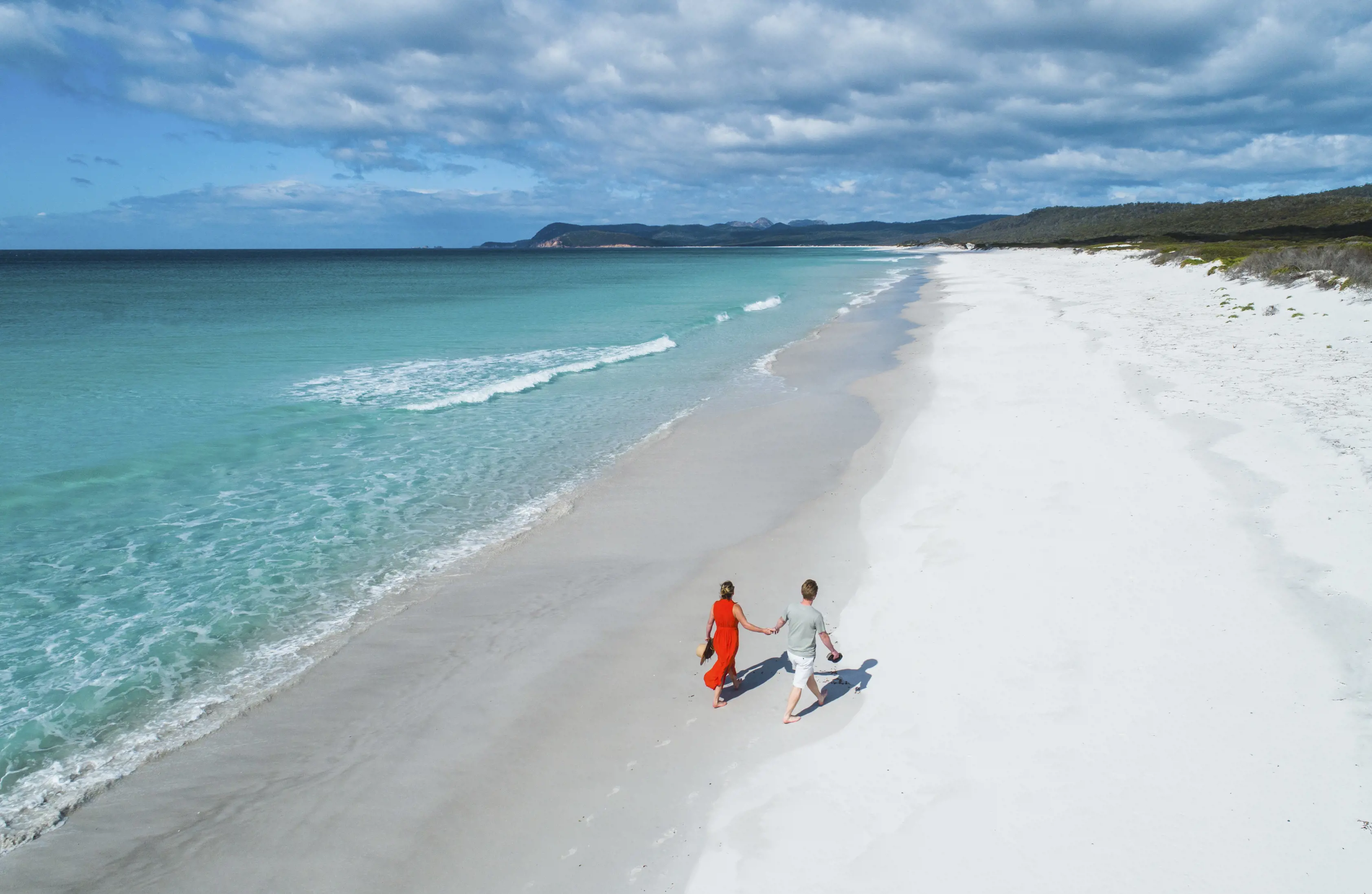 Aerial image of couple walking along the incredible Friendly Beaches, with clear, blue water and pristine white sand.