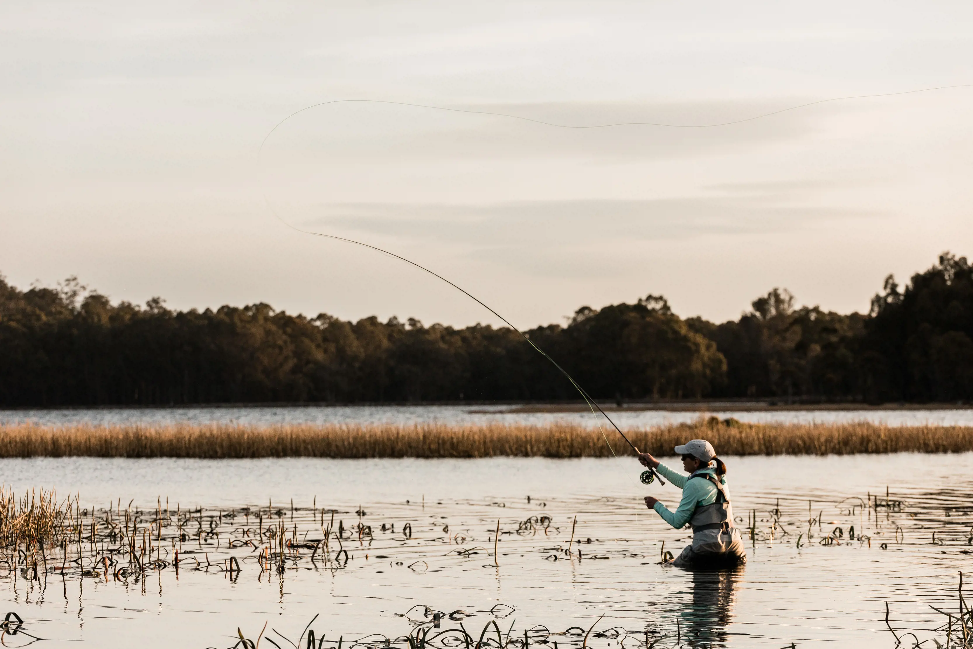 A woman is stood waist deep in the water fly fishing on Penstock Lagoon.