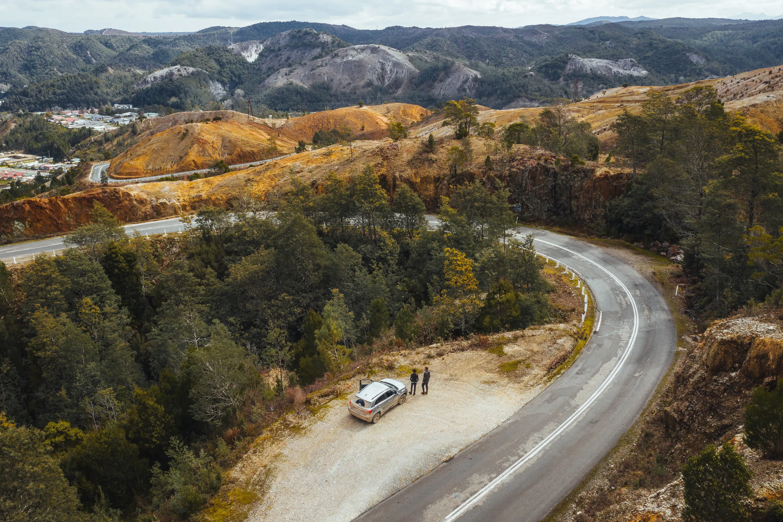 Stunning aerial image of a car parked on the road to Queenstown, surrounded by forest, dramatic hills and mountains.