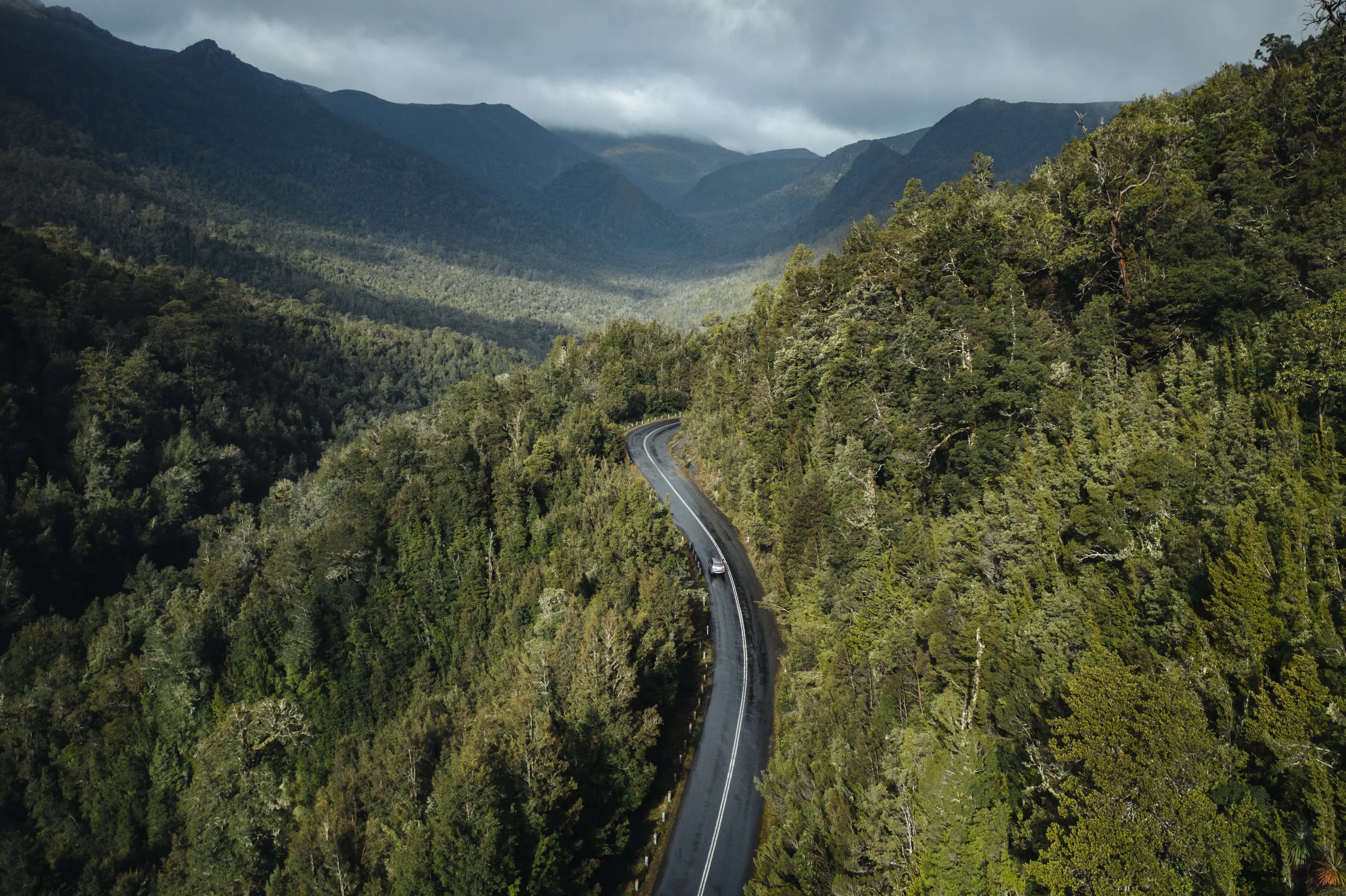 Breathtaking aerial image of a car driving through Surprise Valley, Lyell Highway, surrounded by lush forest and mountains.