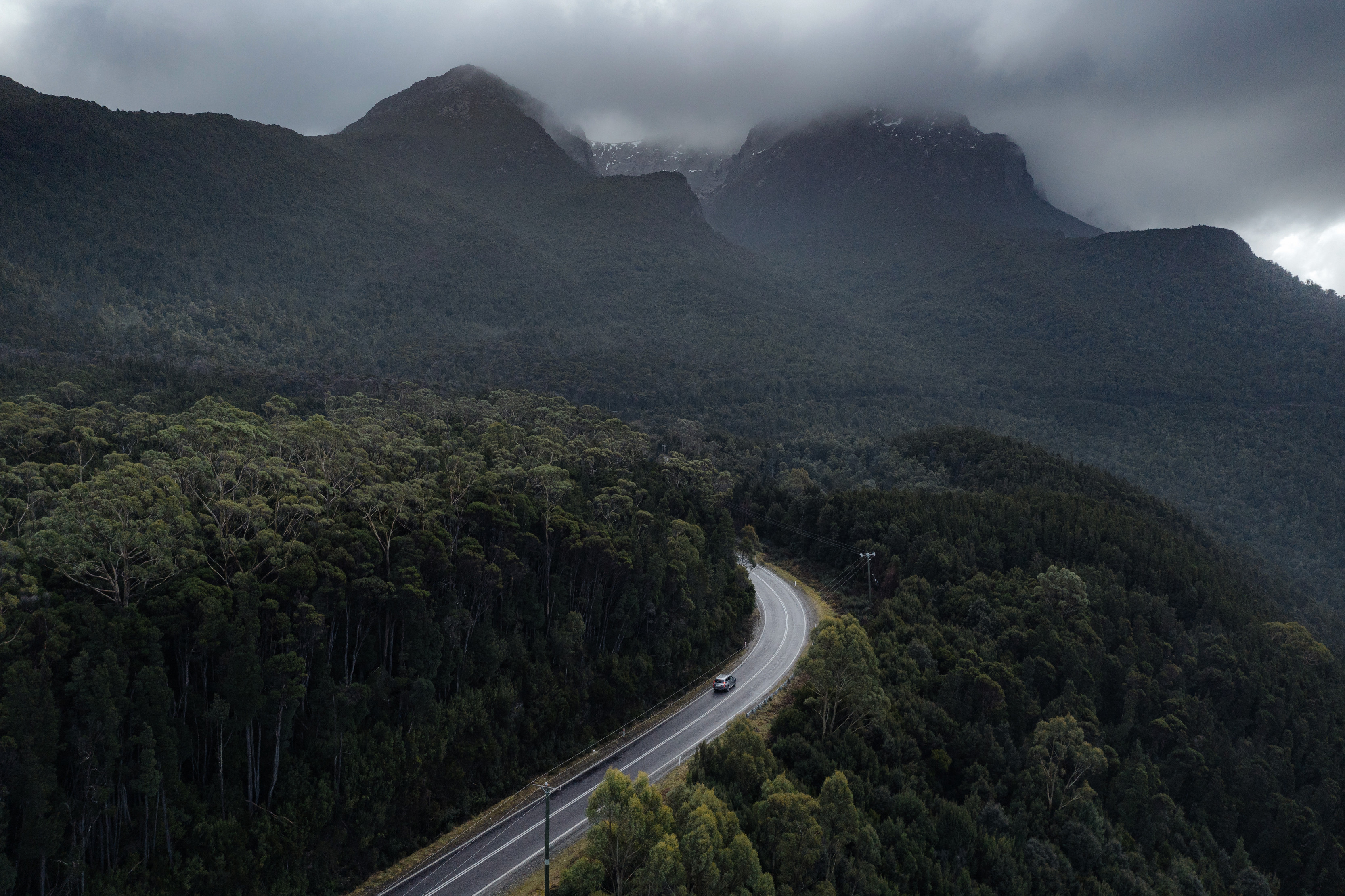 Breathtaking aerial image of a car driving through Mt Murchison from the Anthony Road, surrounded by lush forest and mountains.