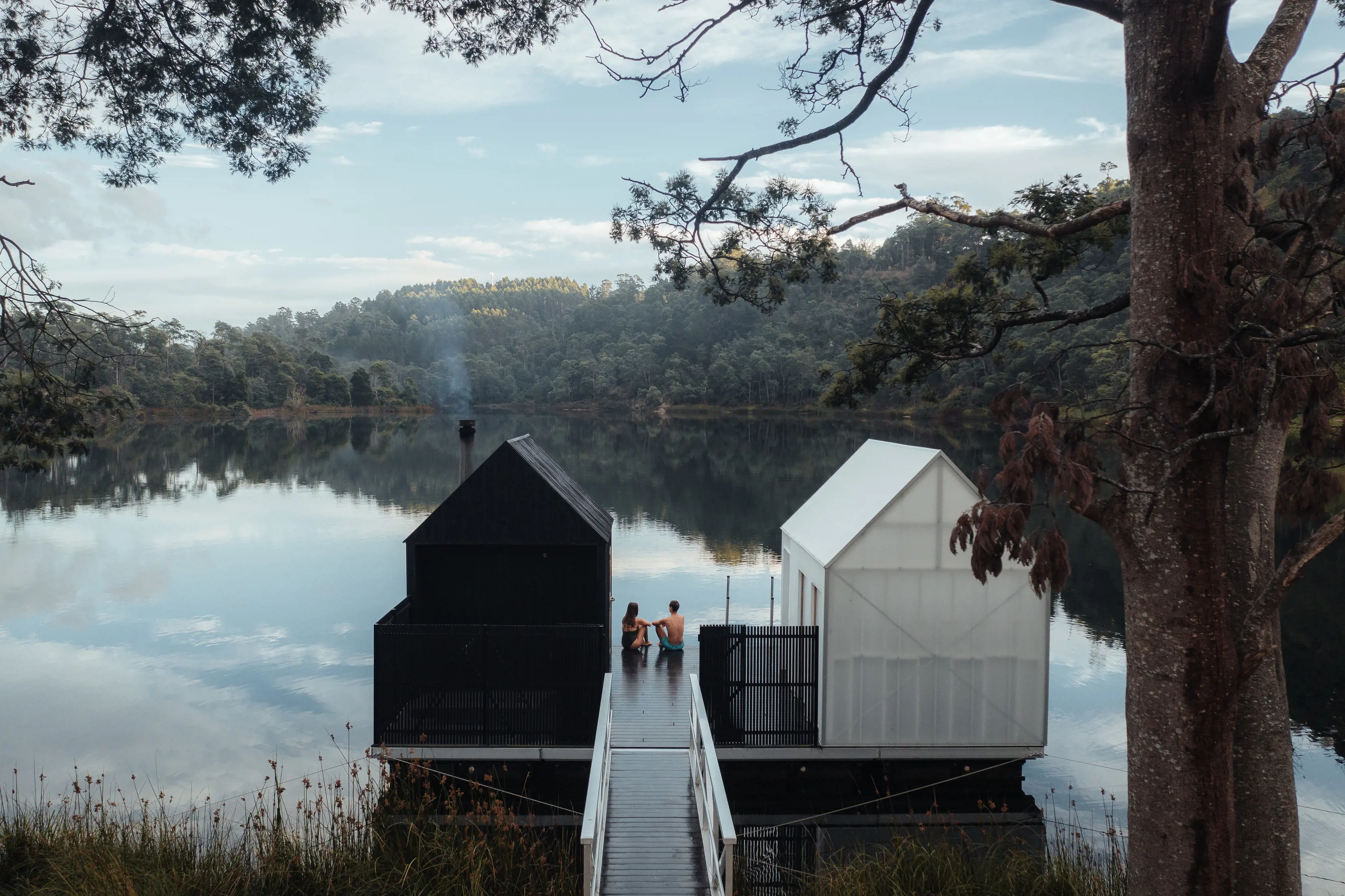 A couple sit on the deck between the waterfront saunas at Floating Sauna Lake Derby.