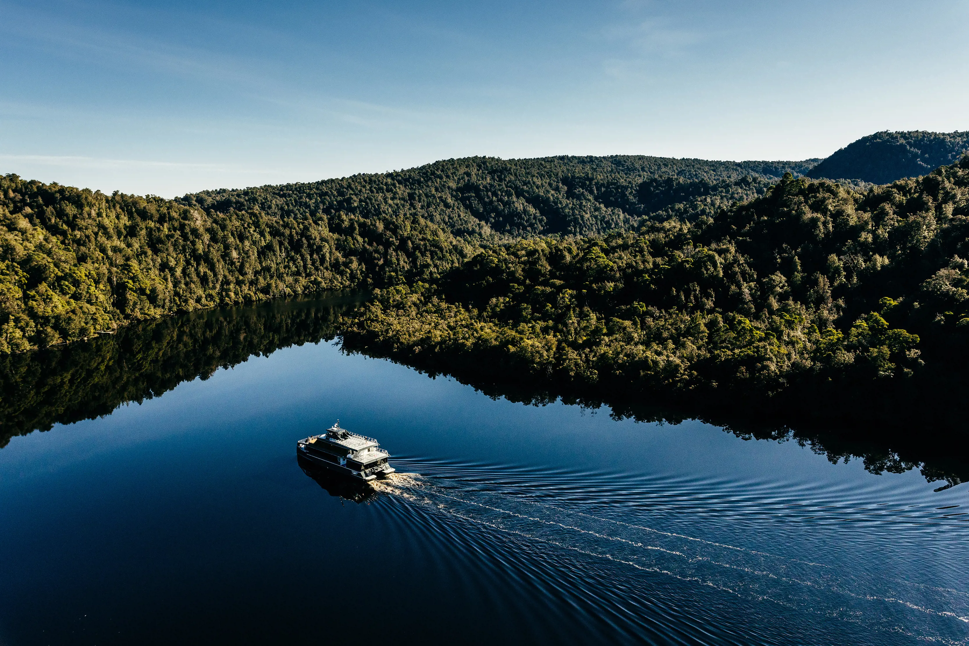 Incredible aerial image of Gordon River Cruises, piloting through Gordon River, surrounded by lush forest on either side of the river.
