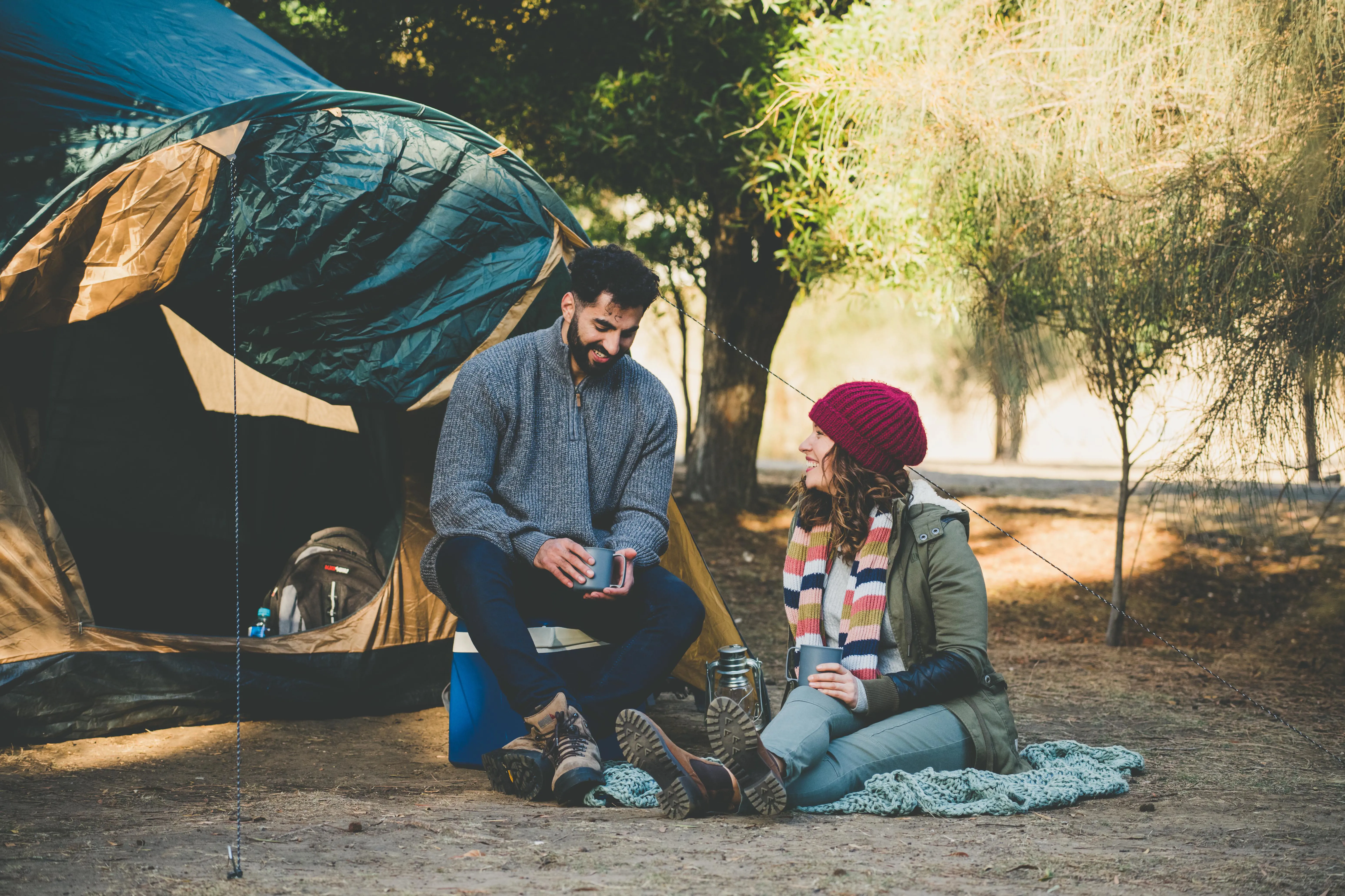 A young couple sit outside their tent on a sunny afternoon.