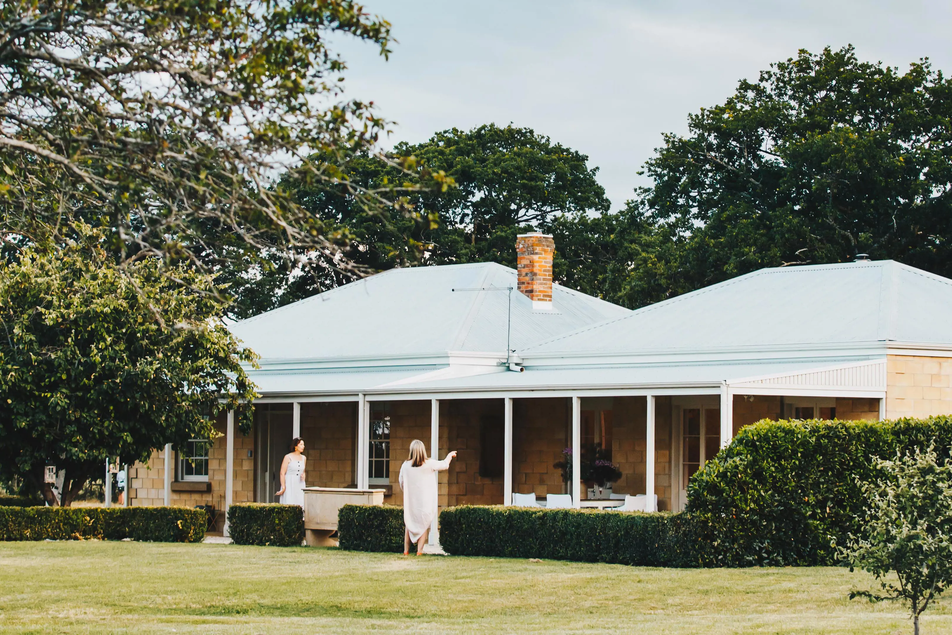 Two people walk the gardens around the perimeter of a heritage building.