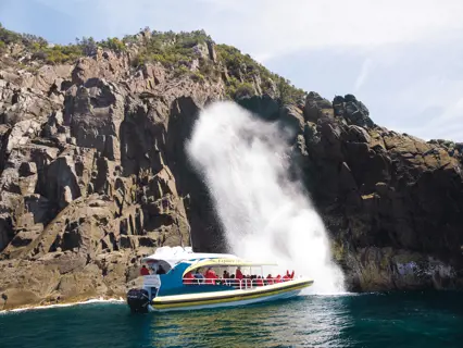 Tourists onboard a boat watching the "Breathing Rock". Water is spitting out from the rocks.