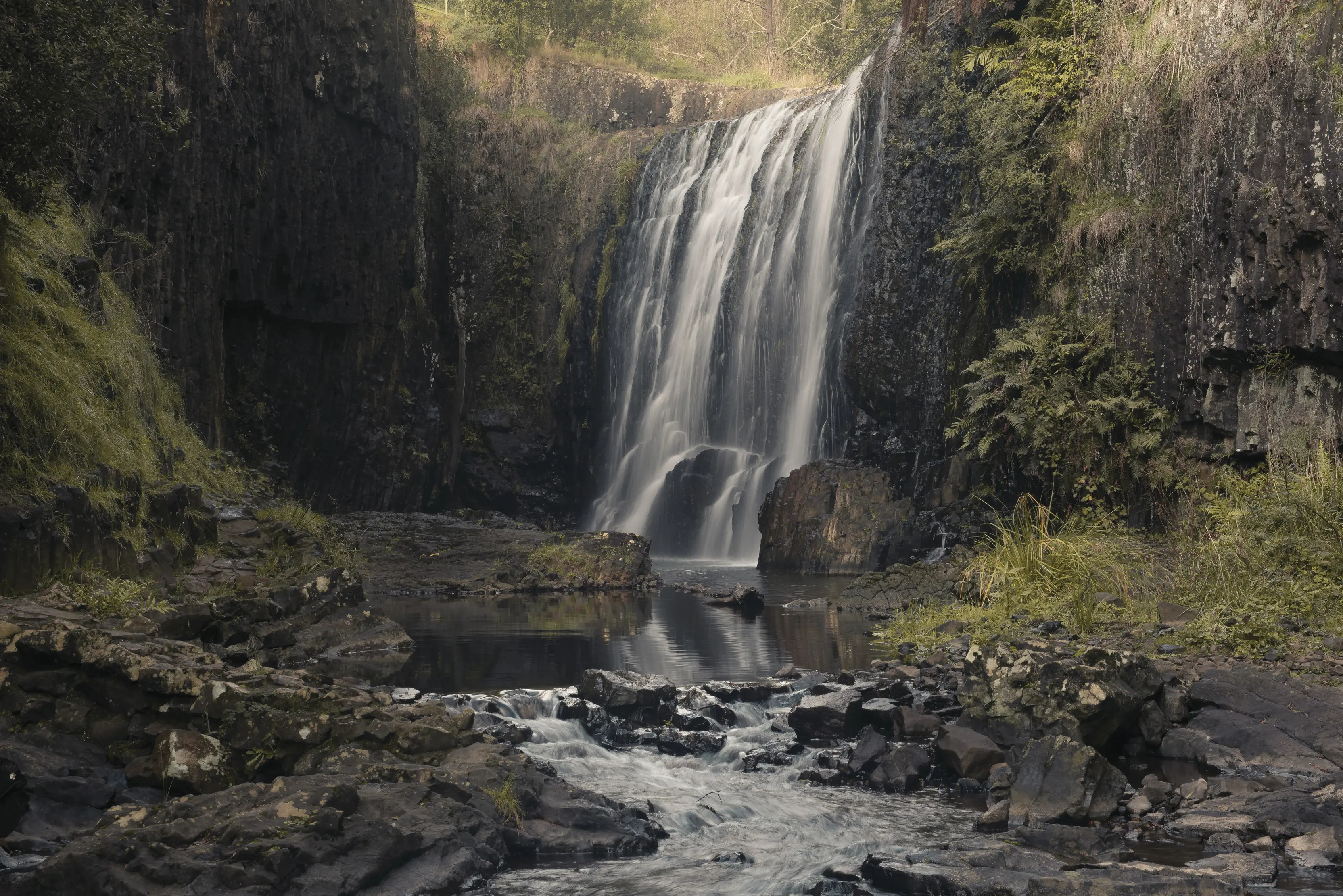 At the base of the beautiful and stunning Guide Falls. Surrounded by rocks and greenery.