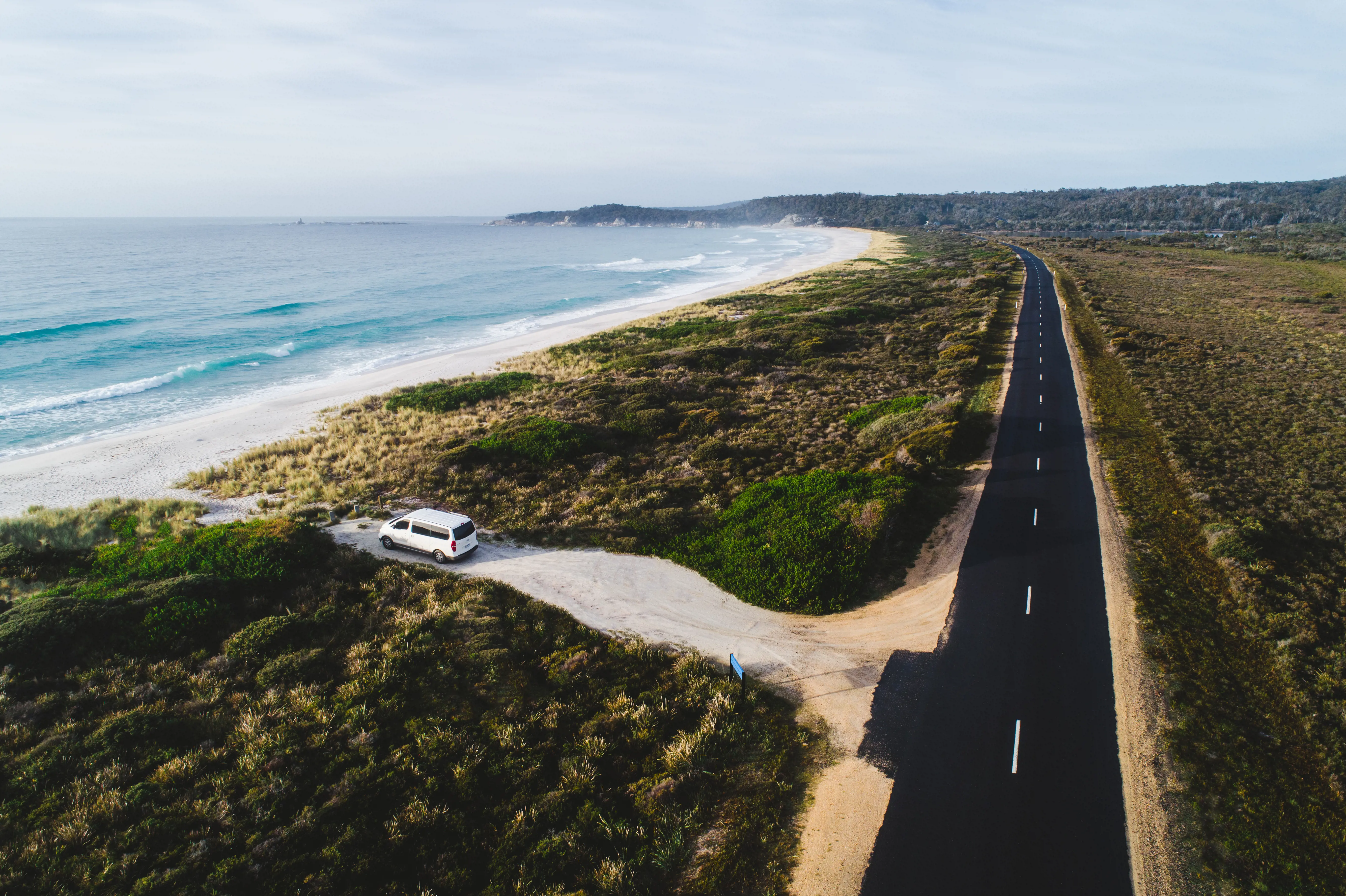 A car pulls up into a parking area near a sandy beach.